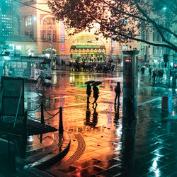 People walking on wet illuminated city at night