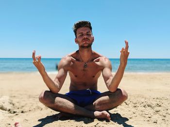 Full length of shirtless man doing yoga at beach against sky