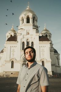 Man with eyes closed against building and sky 