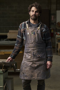 Portrait of confident carpenter wearing apron while standing in workshop