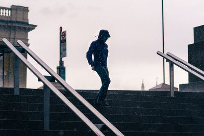 Side view of young woman standing on staircase against sky