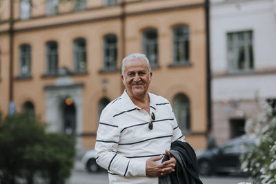 Portrait of smiling senior man with hands clasped at street