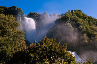 Scenic view of waterfall in forest against sky