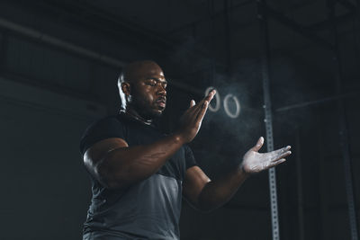 Low angle view of male athlete applying chalk on hands while standing in gym