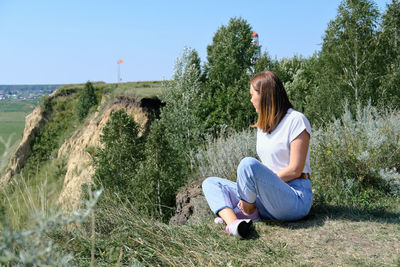 Beautiful woman sitting on a high river bank and looking aside. lonely travel and local travelling 