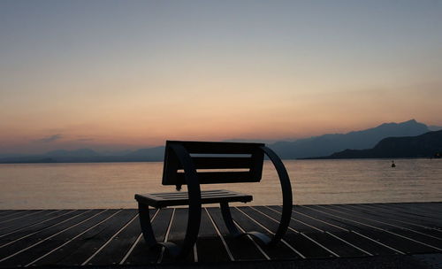 Chair on bench by sea against sky during sunset