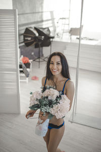 Portrait of female model holding bouquet while standing at home