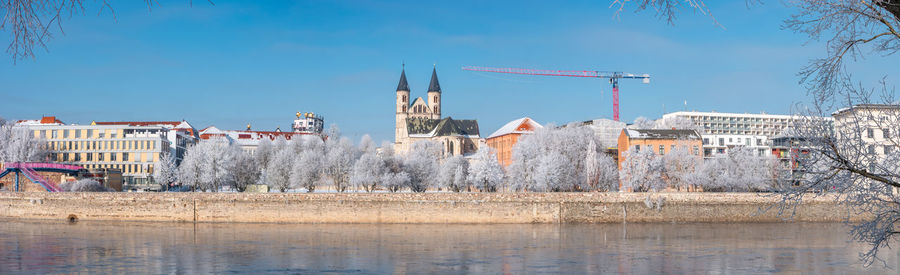 Buildings by river against blue sky