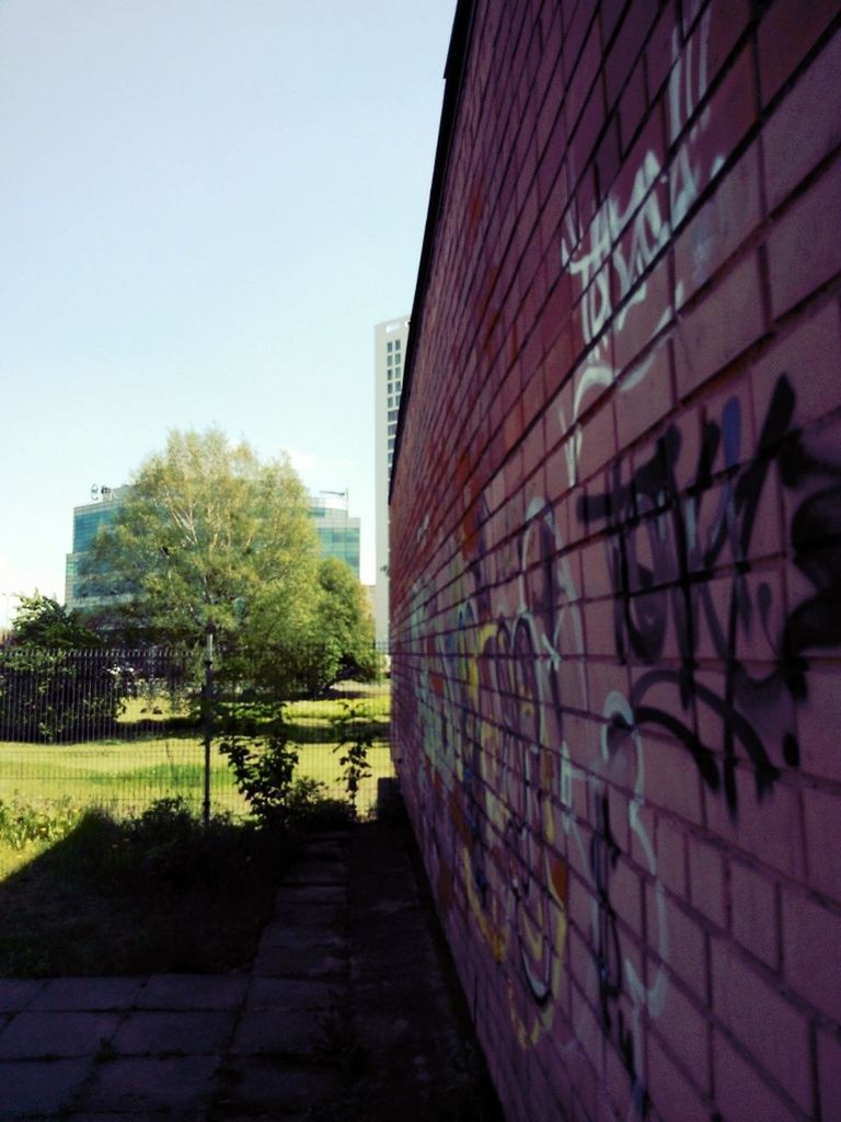 built structure, architecture, building exterior, clear sky, tree, the way forward, wall - building feature, day, graffiti, city, outdoors, grass, footpath, no people, building, pattern, sunlight, walkway, sky, modern