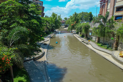 Canal amidst trees and buildings against sky