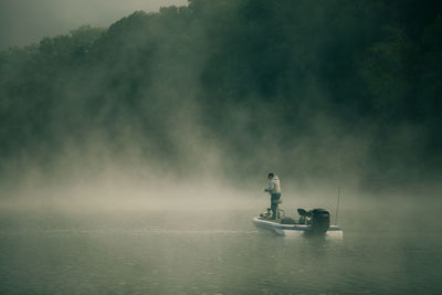 Rear view of man fishing at lake during foggy weather