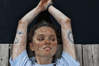 Close-up of woman with arms raised against wood