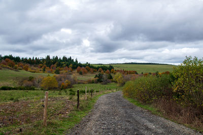 Dirt road amidst field against sky