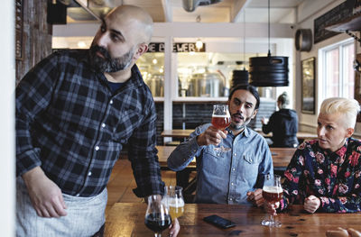 Customers examining various craft beer by bartender at bar