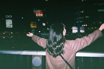 Rear view of woman standing against illuminated city at night