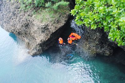 High angle view of friends with life jackets in sea by rocks