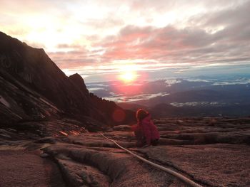 Rear view of woman standing on mountain against sky during sunset
