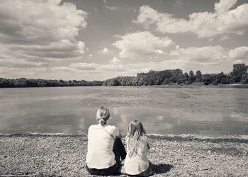 Rear view of couple sitting on lake against sky