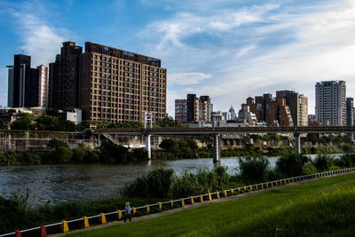 Bridge over river by buildings in city against sky