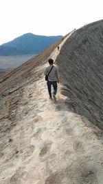 Rear view of man walking on land against sky