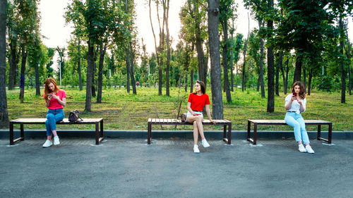 Friends using smart phone while sitting on bench at park