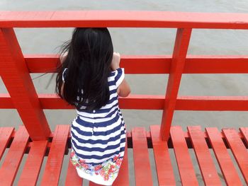 High angle view of girl standing on red footbridge over river