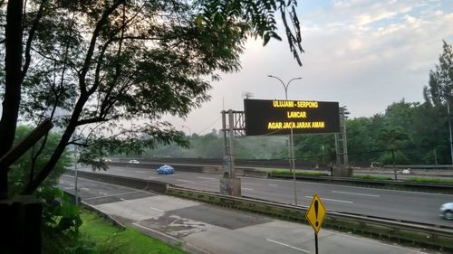 Road sign by trees against sky