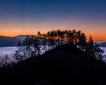 Silhouette trees by lake against sky during sunset