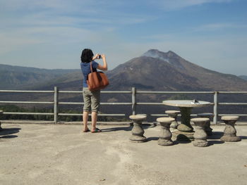 Rear view of woman photographing mountains while standing by railing