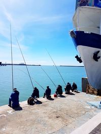 People sitting by sea against blue sky