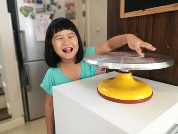 Portrait of cheerful girl touching cakestand on table at home