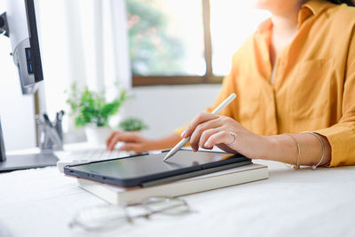 Midsection of man using graphic tablet while sitting on table at home