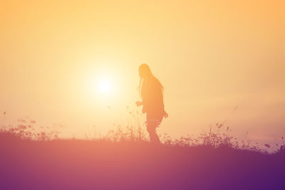 Silhouette man standing on field against orange sky