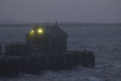 Illuminated building by sea against sky at dusk