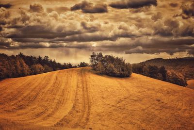 Dirt road passing through landscape against cloudy sky