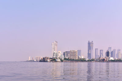 Sea by modern buildings against clear sky