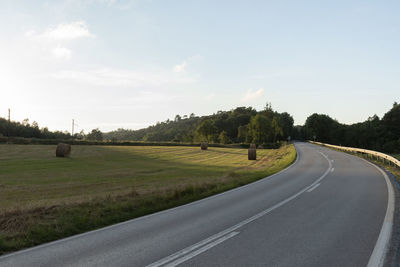 Empty road amidst field against sky