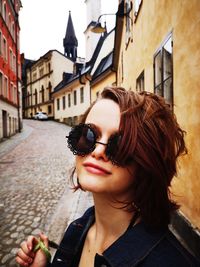 Portrait of girl wearing sunglasses on street amidst buildings in city