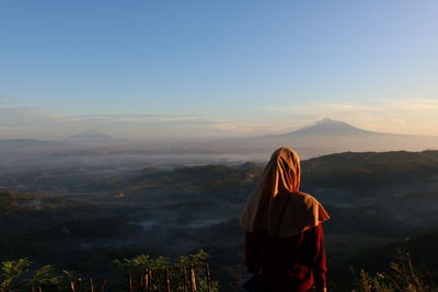 Rear view of man looking at cityscape against sky