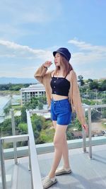 Full length portrait of young woman standing against railing