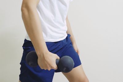 Midsection of man holding dumbbell while standing against wall