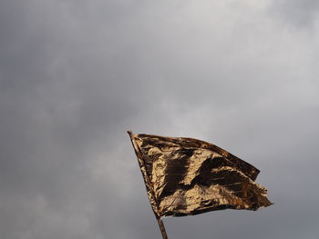 Low angle view of golden shiny flag against cloudy sky