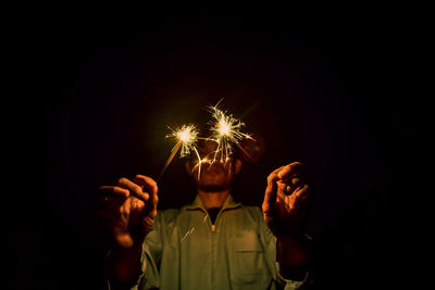 Man holding illuminated sparklers at night