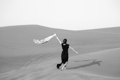 Rear view of woman walking at desert against clear sky