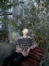 Young man sitting on plant against trees