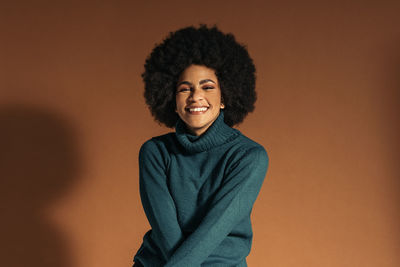 Portrait of young woman standing against brown background
