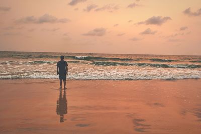 Rear view of man standing at beach during sunset