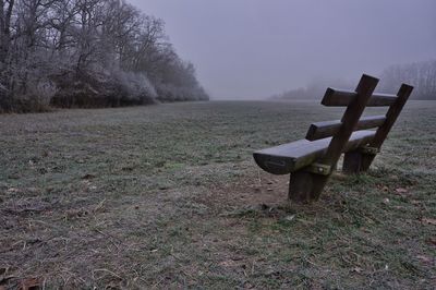 Empty bench on field against sky