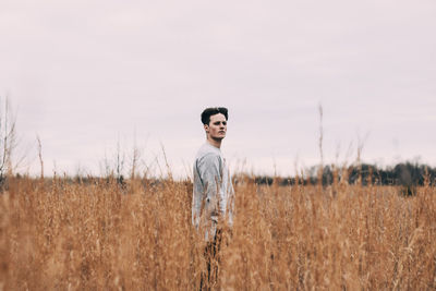 Side view of young man standing on field against clear sky