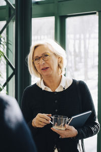 Senior businesswoman holding cup while looking at male colleague in office